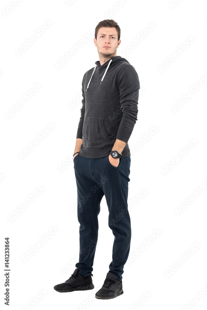 Serious frowning man in sportswear with hands in pockets looking at camera. Full body length portrait over white studio background. Serious frowning man in sportswear with hands in pockets looking at camera. Full body length portrait over white studio background.