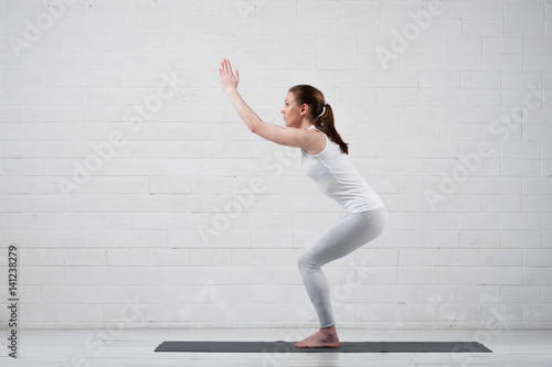 Young flexible woman doing yoga against white wall