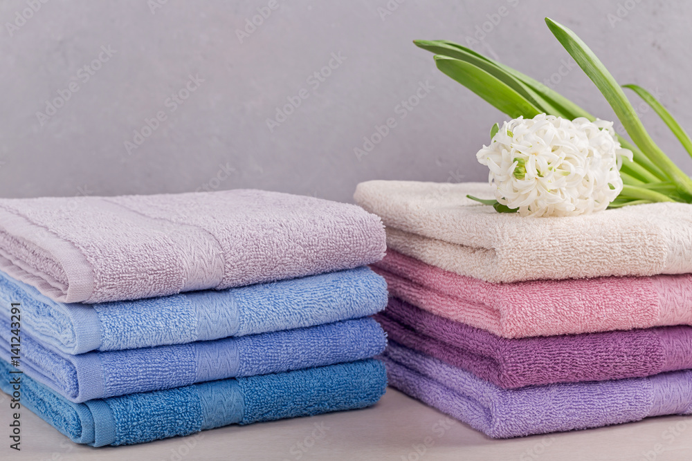 Two stacks of colorful bath towels with hyacinth flower on light background. Two stacks of colorful bath towels with hyacinth flower on light background.