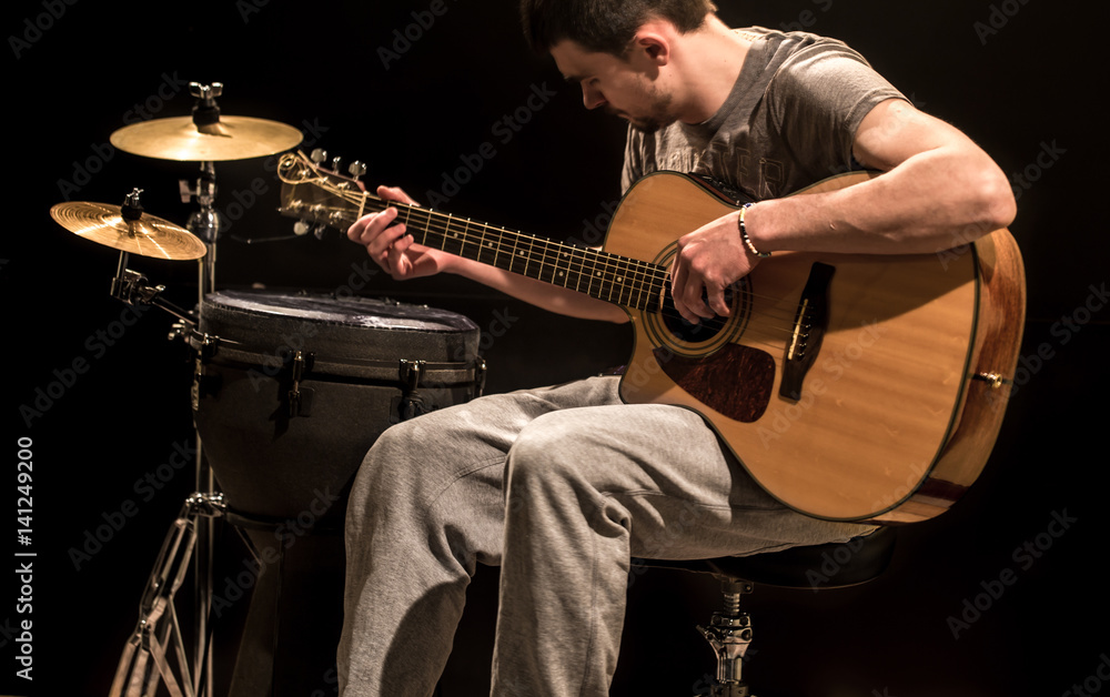 Fototapeta premium musician plays acoustic guitar and percussion instruments, black background