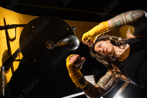 Concentrated woman doing a fitness boxing workout with a punching bag. The girl in the boxing hall emotionally beats the boxing bag photo