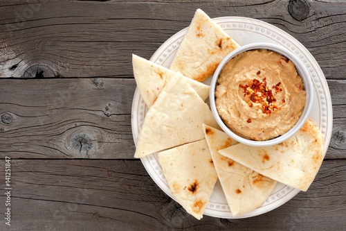 Hummus dip with pita bread on a plate, above view on a rustic wooden background