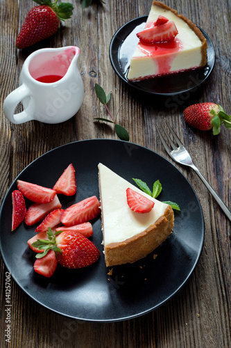 Two slices of strawberry cheesecake  strawberry sauce and fresh strawberries on a plate over rustic wooden table. High angle view  vertical image