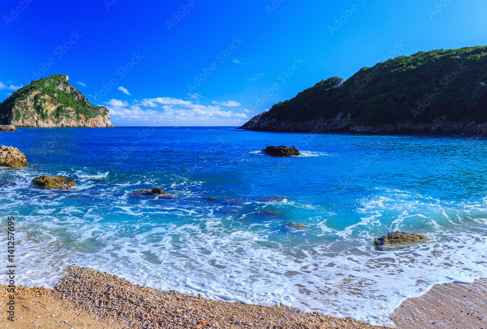 Beautiful summer panoramic seascape. View of the coastline into the sea bays with crystal clear azure water. Foam wave at the beach with shingle. Paleokastrica. Corfu. Ionian archipelago. Greece.