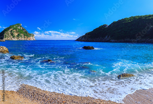 Beautiful summer panoramic seascape. View of the coastline into the sea bays with crystal clear azure water. Foam wave at the beach with shingle. Paleokastrica. Corfu. Ionian archipelago. Greece.