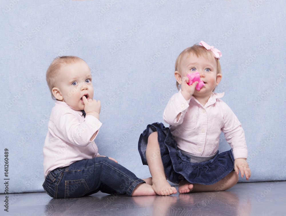 Lovely infant boy and funny baby girl sitting on the floor and looking at camera man Lovely infant boy and funny baby girl sitting on the floor and looking at camera man
