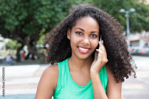 Laughing latin woman with curly hair and green shirt at phone in city