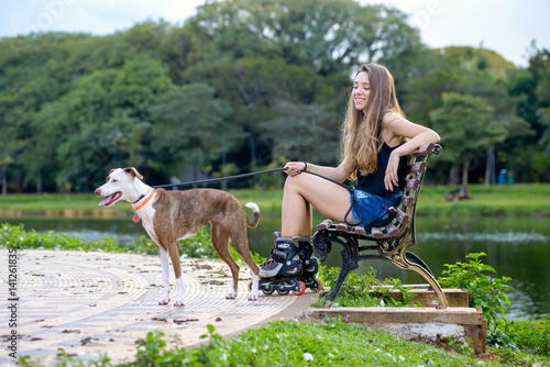woman with inline roller skates sitting down on a bench with a dog © Elayne