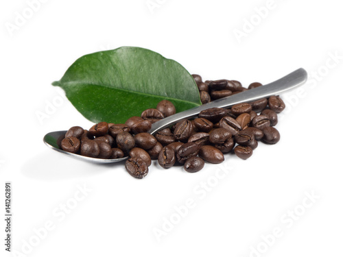 Pile of coffee grains with silver spoon and green leaf over white isolated background.