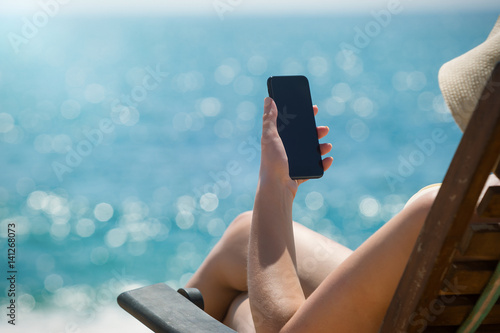 Obraz na plátne Young girl lying on a beach lounger with mobile phone in hand on the tropical is