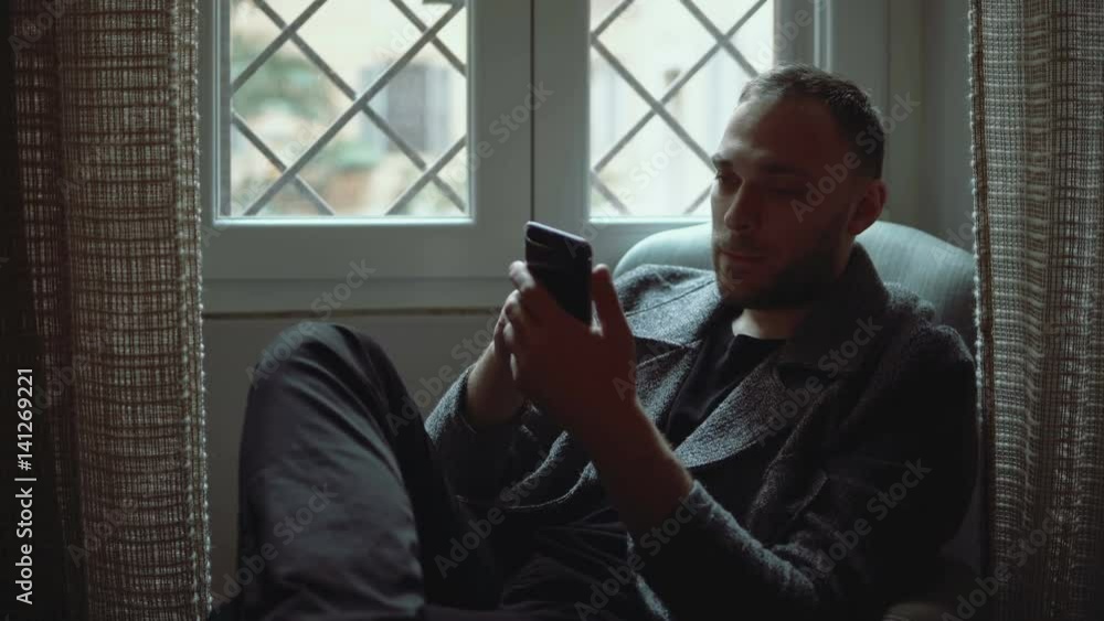 Portrait of attractive man sitting in armchair in living room and using smartphone. Stylish businessman browse Internet. Portrait of attractive man sitting in armchair in living room and using smartphone. Stylish businessman browse Internet.