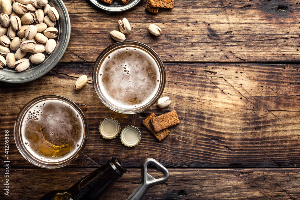 Two glasses of fresh beer and salty snacks on a brown wooden table, top view and space for text Two glasses of fresh beer and salty snacks on a brown wooden table, top view and space for text