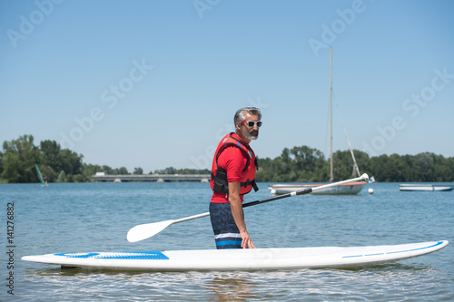 man next to a stand-up paddle board on the lake