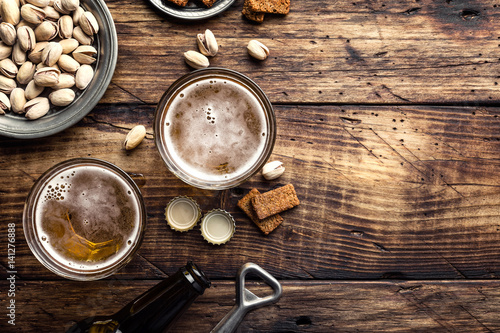 Two glasses of fresh beer and salty snacks on a brown wooden table, top view and space for text