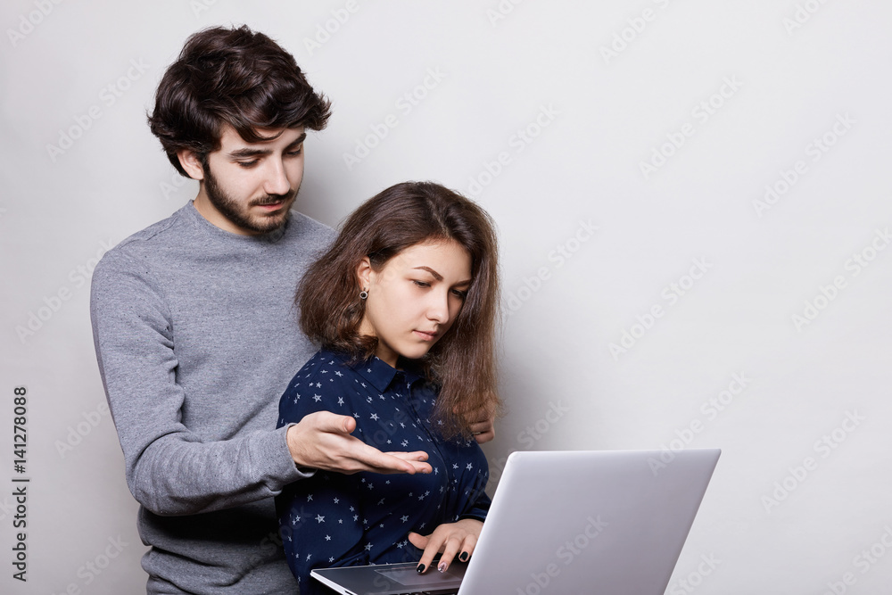 Beautiful girl woman, enjoying modern technologies, using her laptop for writing her diploma paper. A stylish bearded student trying to help her friend pointing with his arm into the screen. Beautiful girl woman, enjoying modern technologies, using her laptop for writing her diploma paper. A stylish bearded student trying to help her friend pointing with his arm into the screen.