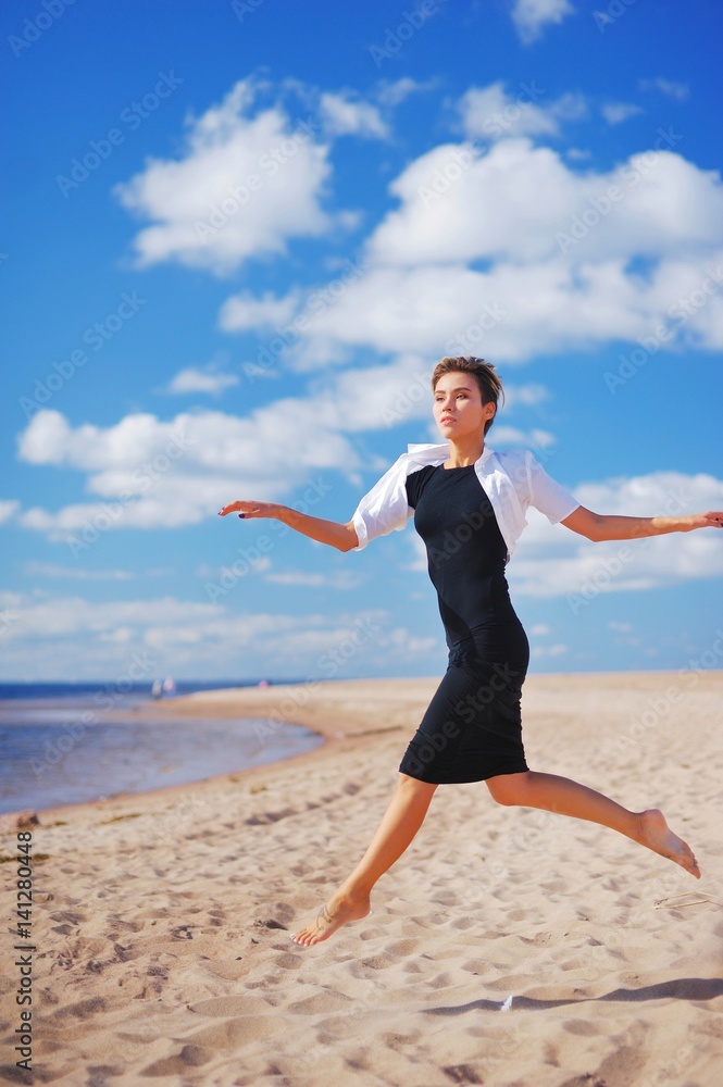 Magnificent portrait of young slim woman in a black dress with a white Bolero, running barefoot on the sand to the sea on the background of blue sky and floating on it white clouds. Magnificent portrait of young slim woman in a black dress with a white Bolero, running barefoot on the sand to the sea on the background of blue sky and floating on it white clouds.