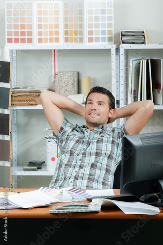 Man sat at desk, leaning back hands behind his head photo