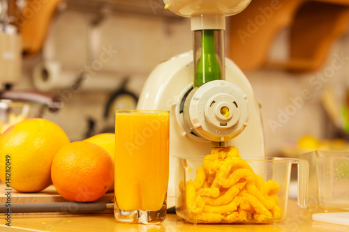 Making orange juice in juicer machine in kitchen
