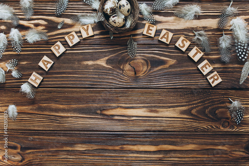 Decoration with quail eggs, nest and feathers. Vintage wooden background with sample text Happy Easter.