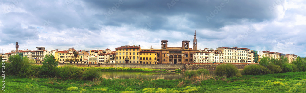 Beautiful panoramic view of Florence riverside, Arno River, National Library in the middle, green grass in foreground and majestic powerful cloudy sky