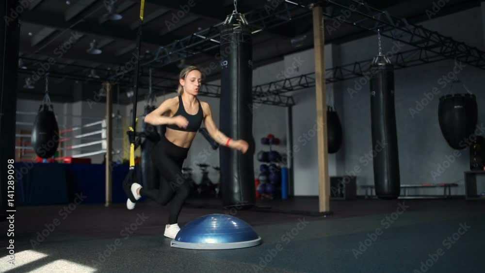 Fit woman in black sportswear doing push UPS on the Bosu and the TRX in gym Fit woman in black sportswear doing push UPS on the Bosu and the TRX in gym