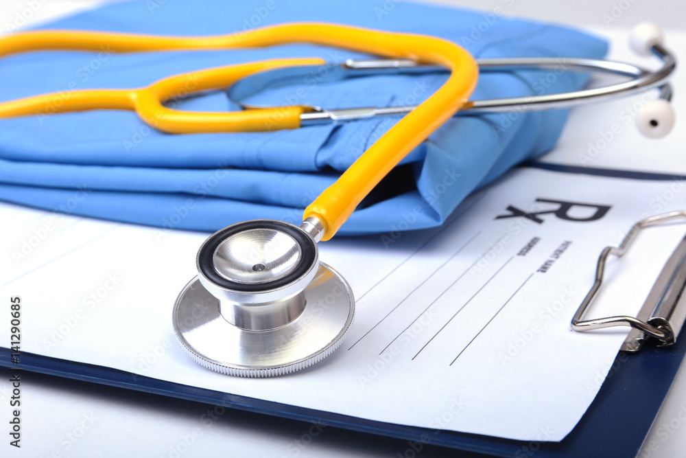 Medical stethoscope, Gloves, RX prescription on blue doctor uniform closeup. Medical tools and instruments shop, therapeutist workspace, physical, blood pressure measurement concept Medical stethoscope, Gloves, RX prescription on blue doctor uniform closeup. Medical tools and instruments shop, therapeutist workspace, physical, blood pressure measurement concept