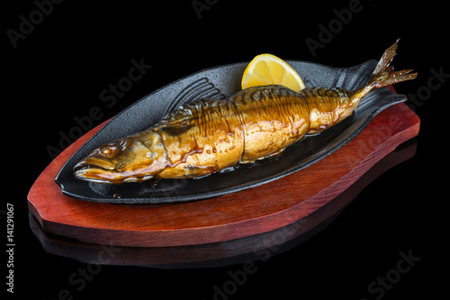 Mackerel cooked in a grill. Served in a black frying pan, on a black background with reflection.
