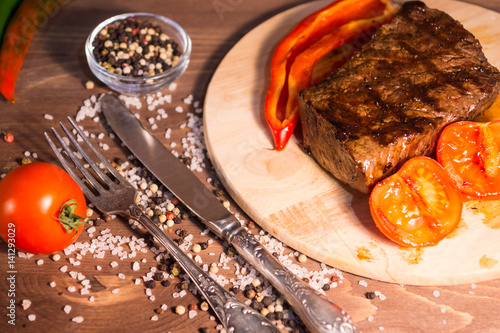 Beef steak with baked peppers and tomatoes on a wooden board