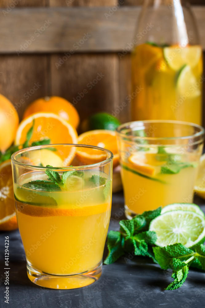 Healthy citrus lemonade from oranges, fresh mint, lime in glasses and bottle on dark stone kitchen table Healthy citrus lemonade from oranges, fresh mint, lime in glasses and bottle on dark stone kitchen table