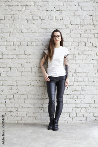 Young tattooed woman wearing blank t-shirt, standing in front of brick wall in loft