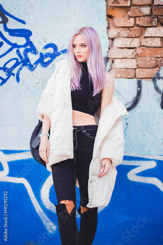 A beautiful girl with purple hair walks the streets of the city. Wearing a jacket, torn jeans