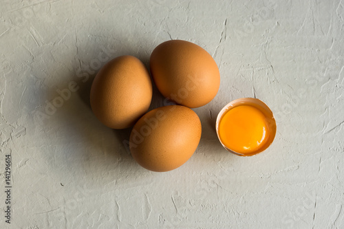 Fresh organic brown eggs, cracked shell, open bright yolk on white concrete table surface, top view, abstract, conceptual