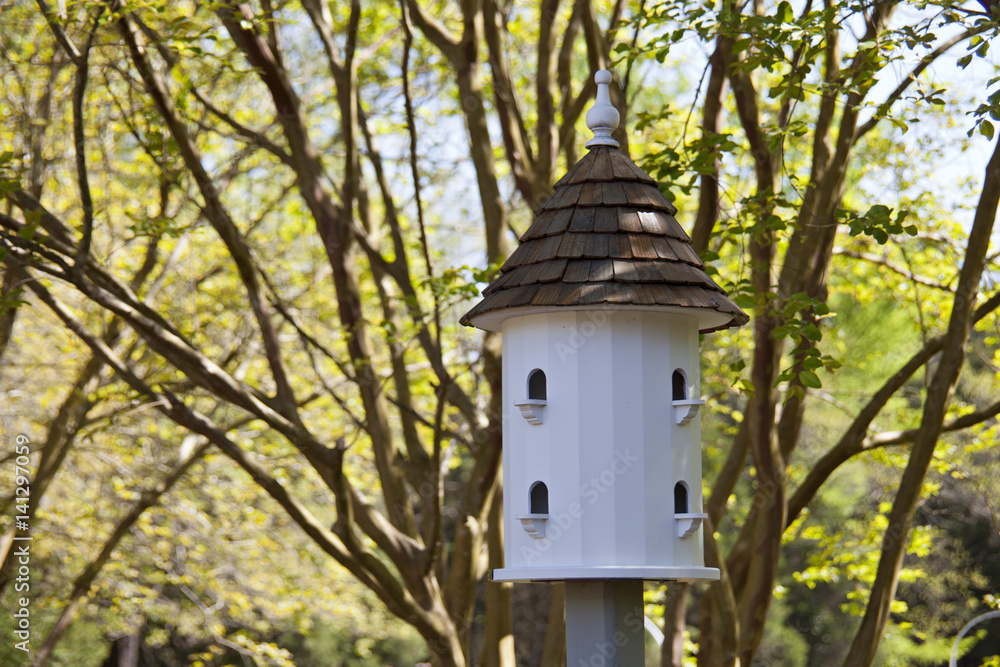 Large, white birdhouse surrounded by lush green trees.