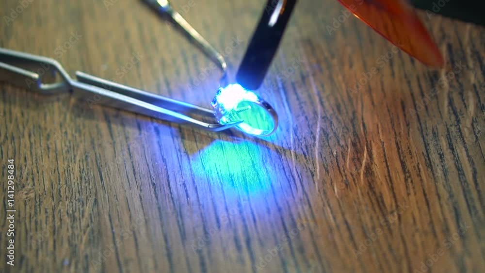 Process of the drying of the enamel layer using an ultraviolet device on the silver ring on the wooden table Process of the drying of the enamel layer using an ultraviolet device on the silver ring on the wooden table