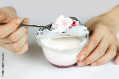 Girl's hand stirred with a spoon of natural yogurt and red jam. Yogurt on the spoon close up. Isolated on white background