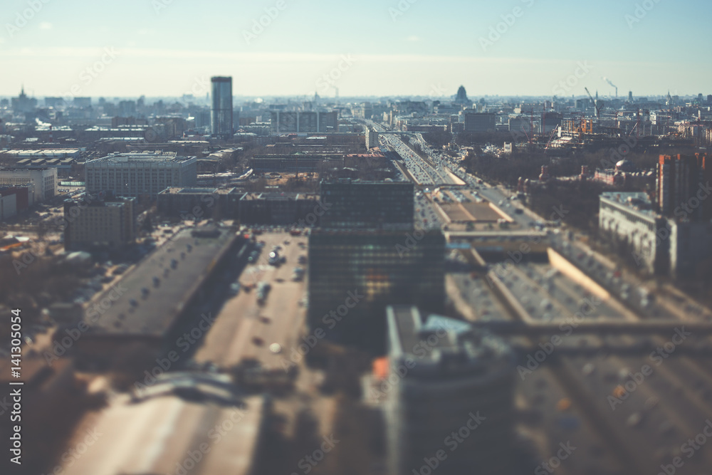 Fototapeta premium True tilt shift shooting of highway in metropolis from high above: multiple residential and office buildings, road intersection in focus with many cars on busy streets of the city, crosstown traffic