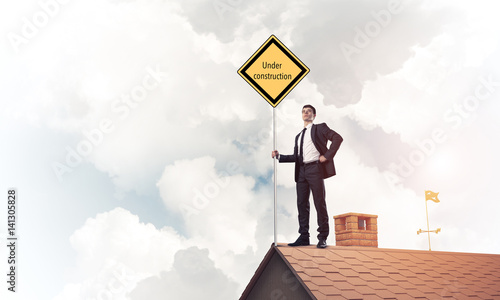 Young businessman on house brick roof holding yellow signboard.  © adam121