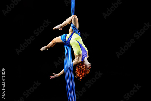 Beautiful young, athletic sexy woman professional aerial circus artist with redhead in yellow costume make coup in the air, light in the darkness. Dancing in the air with balance.