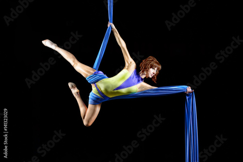 Beautiful young, athletic sexy woman professional aerial circus artist with redhead in yellow costume posing diagonal in the air, light in the darkness. Dancing in the air with balance.