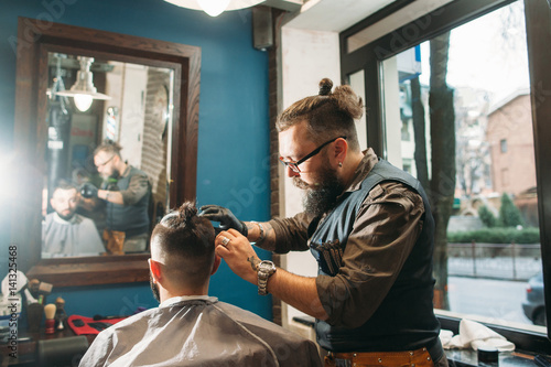 Senior barber finishing stylish hairdo free space. Bearded hairtician cut man, workplace interior background. Beauty, style, modern life, barbershop concept photo