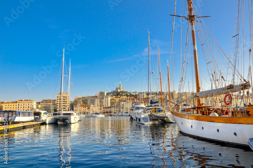 View of pier in the city of Marseille, a set of yachts lie alongside. On other side of the gulf city constructions