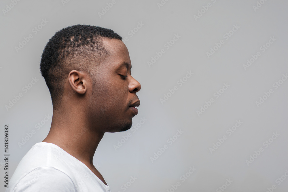Obraz premium Concentrated african man with closed eyes on grey background with free space. Deep concentration, yoga, meditation. Profile view.
