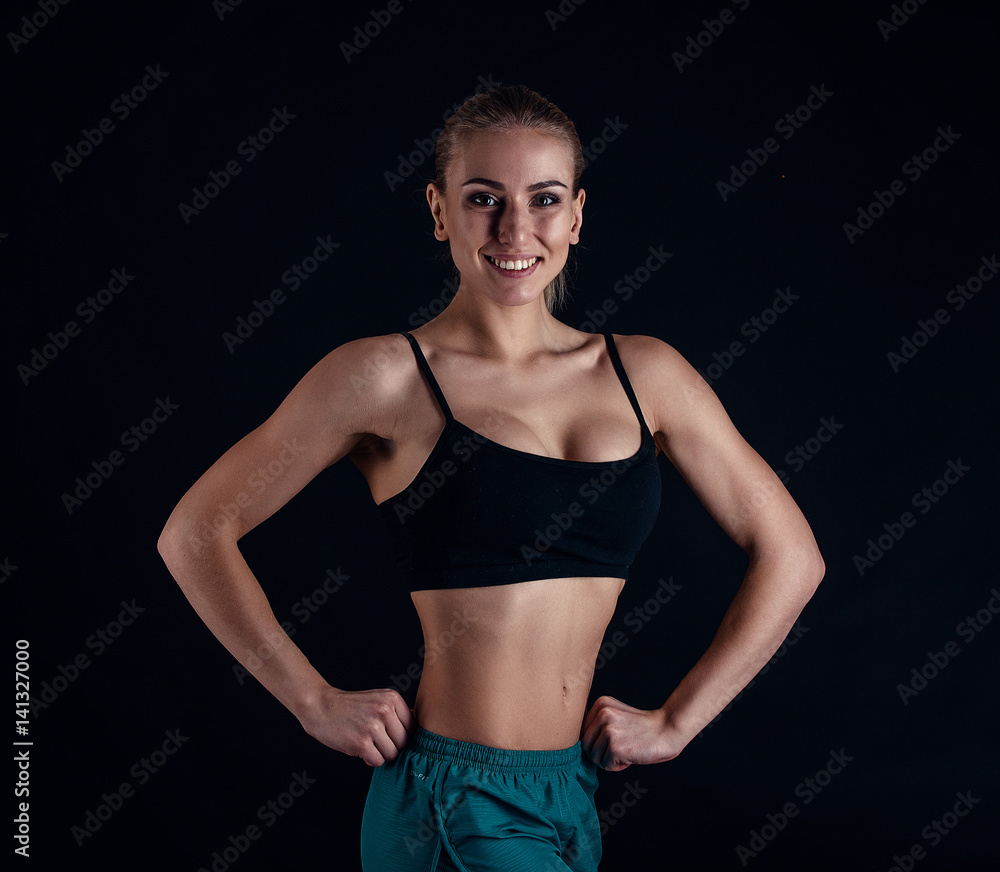 Obraz premium Sporty young girl in sportswear showing muscles on black background. Tanned young athletic woman. A great sport female body.