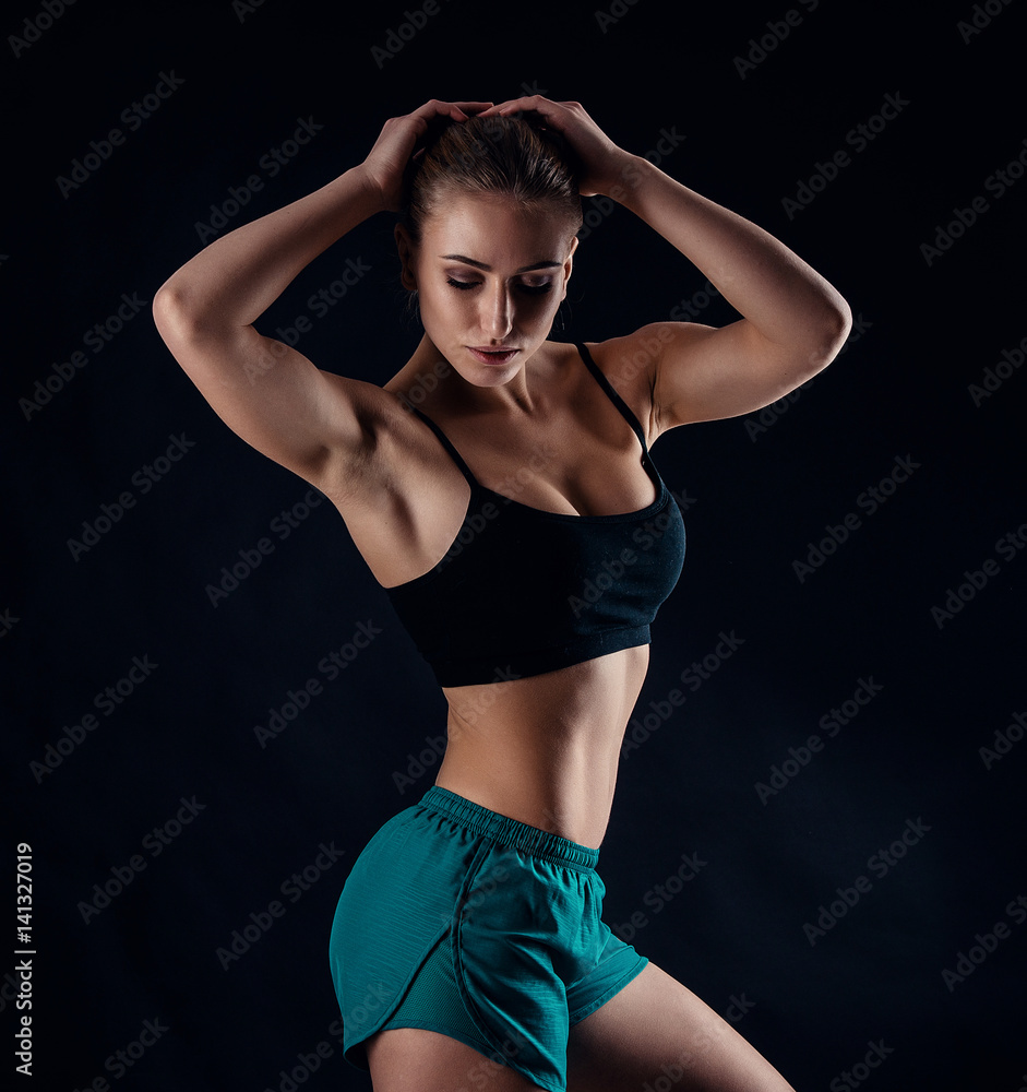 Sporty young girl in sportswear showing muscles on black background. Tanned young athletic woman. A great sport female body. Sporty young girl in sportswear showing muscles on black background. Tanned young athletic woman. A great sport female body.
