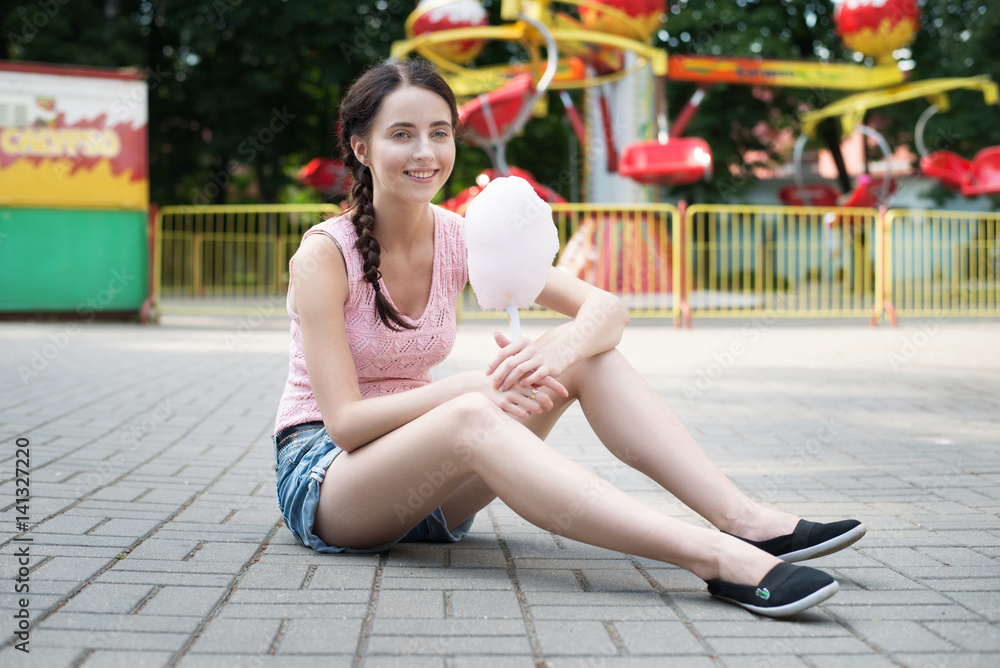 Cute caucasian girl in amusement park is eating pink candyfloss. Portrait of happy attractive young woman with cotton candy. Cute caucasian girl in amusement park is eating pink candyfloss. Portrait of happy attractive young woman with cotton candy.