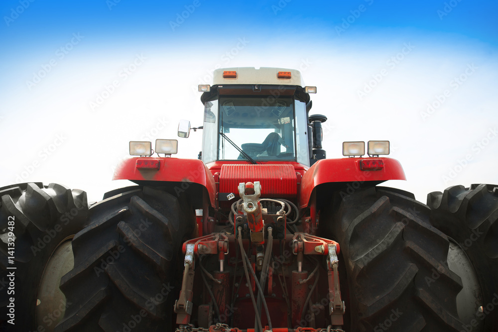 Obraz premium Modern red tractor on a blue sky background.
