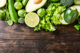 Background with assorted green vegetables, salad, avocado, cucumber, lime and Brussels sprouts on wooden table top. Healthy food concept with copy space.