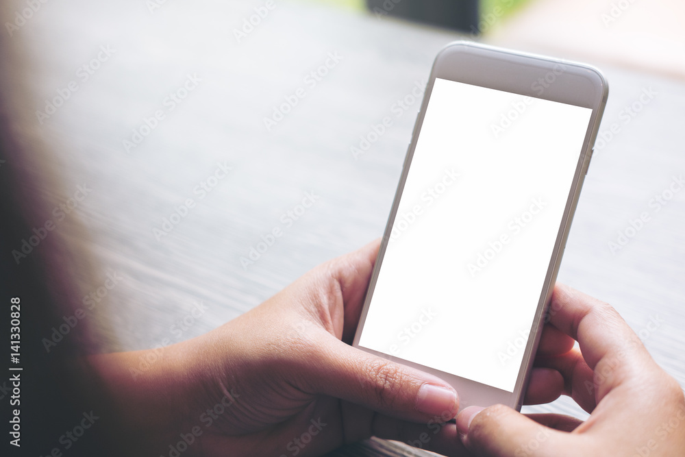 Mockup image of hand holding white mobile phone with blank white screen on vintage wood table in cafe Mockup image of hand holding white mobile phone with blank white screen on vintage wood table in cafe