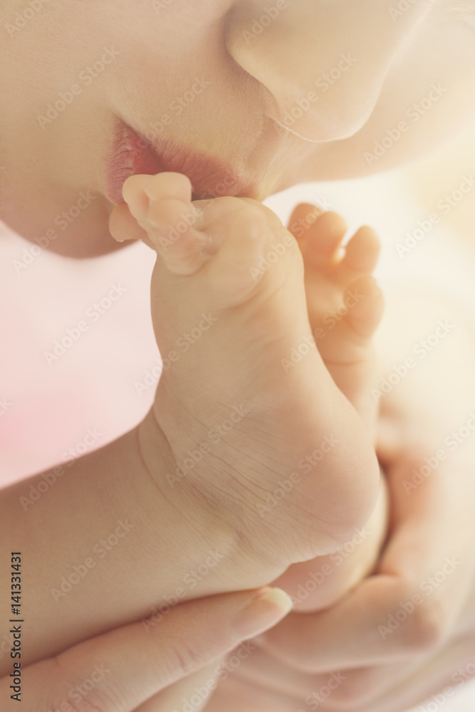 Mother kisses baby feet, closeup. Daylight. Selective focus. Mother kisses baby feet, closeup. Daylight. Selective focus.