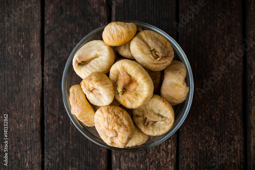 Dried figs in glass bowl on wooden background.